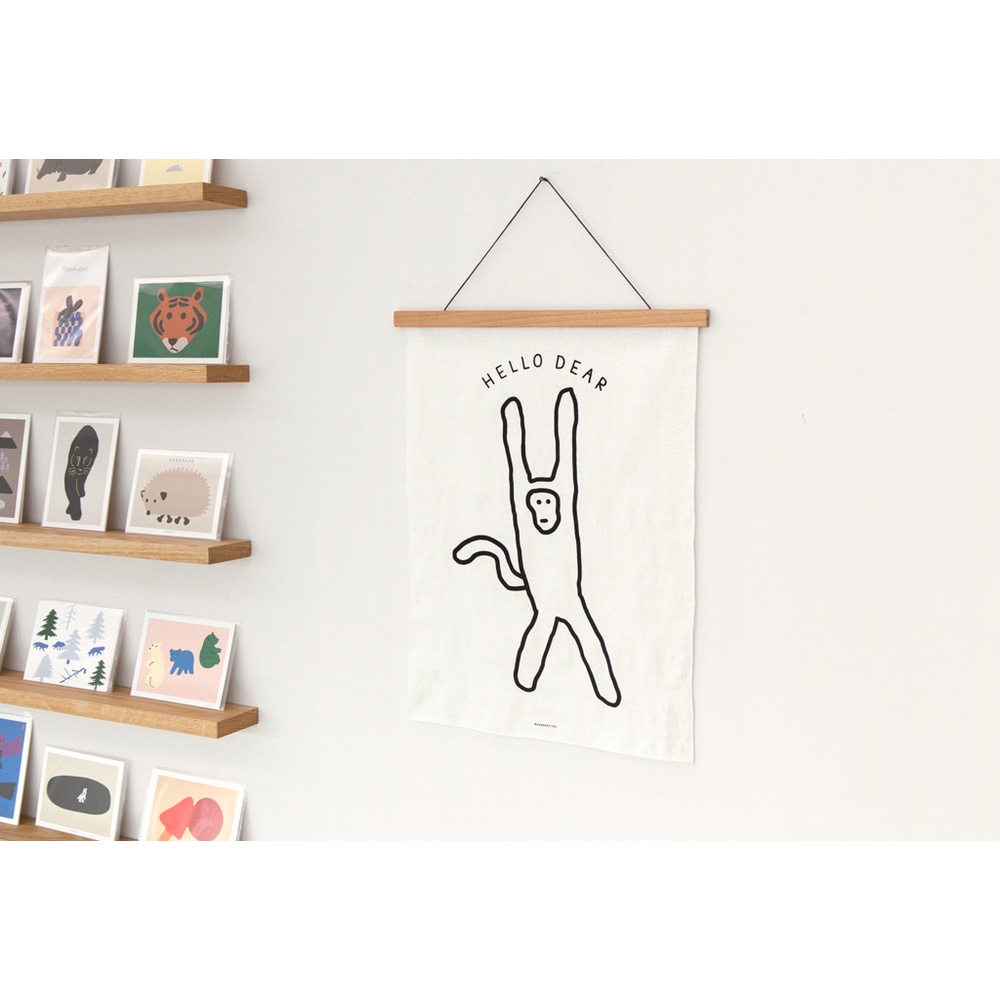 Textilposter Monkey an einer weissen Wand mit duennen Wandleisten auf denen verschiedene Warmgreytail Postkarten stehen.
