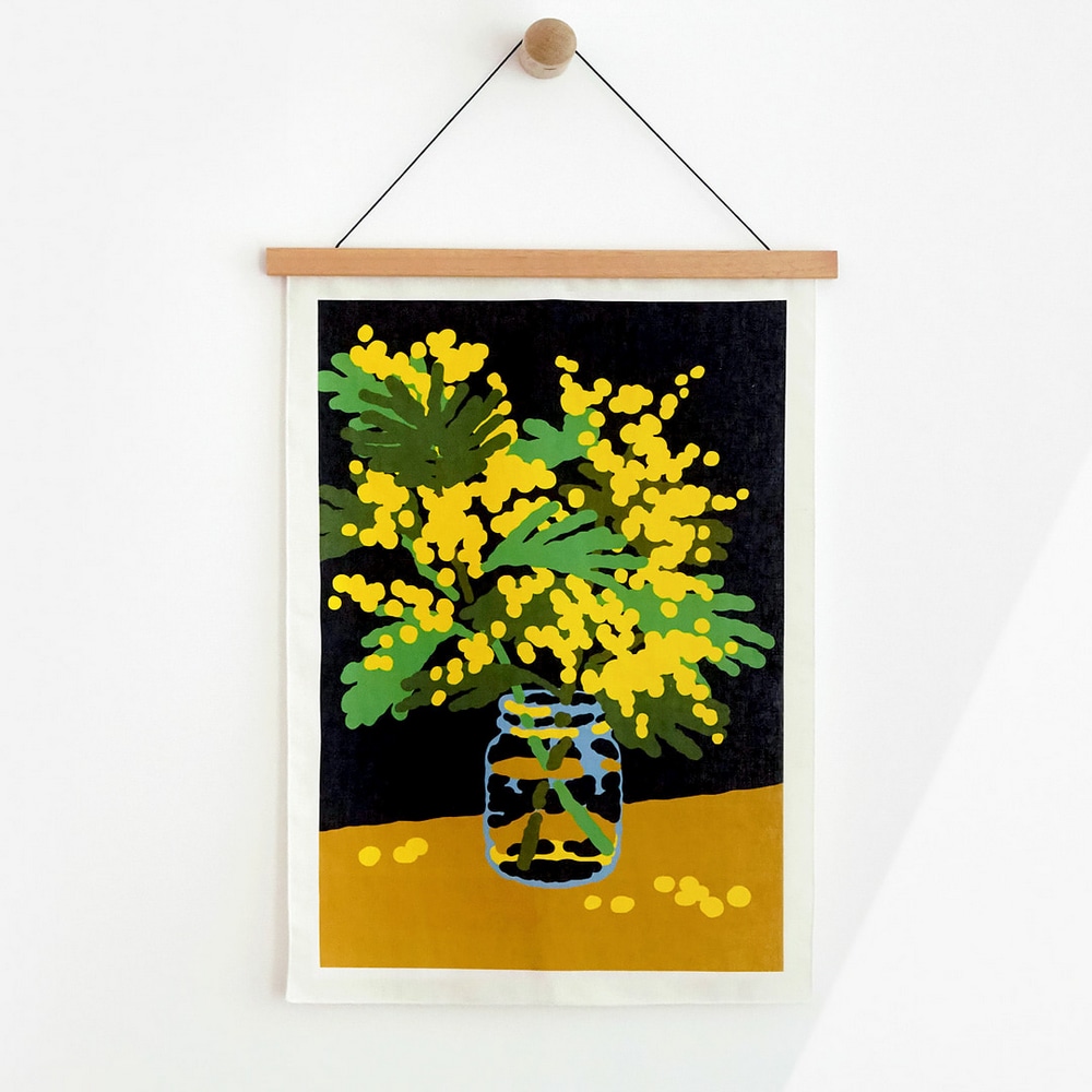 Stoffposter Mimosa, mit gelben Mimosen in einem Einmachglas, mit einer hellen Holzleiste aufgehaengt.
