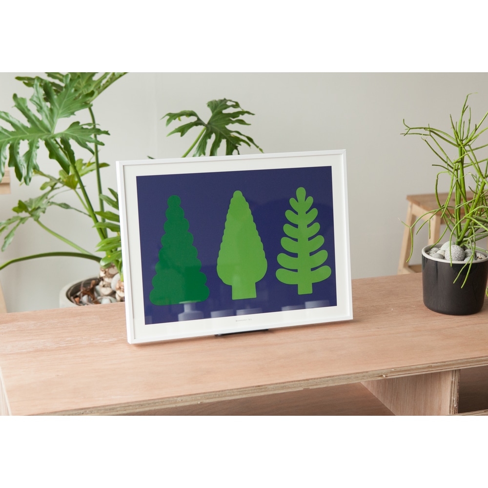 Weiss gerahmter Kunstdruck Tree and Tree mit drei gruenen Tannenbaeumen auf heller Holzkonsole mit Gruenpflanzen im Zimmer.