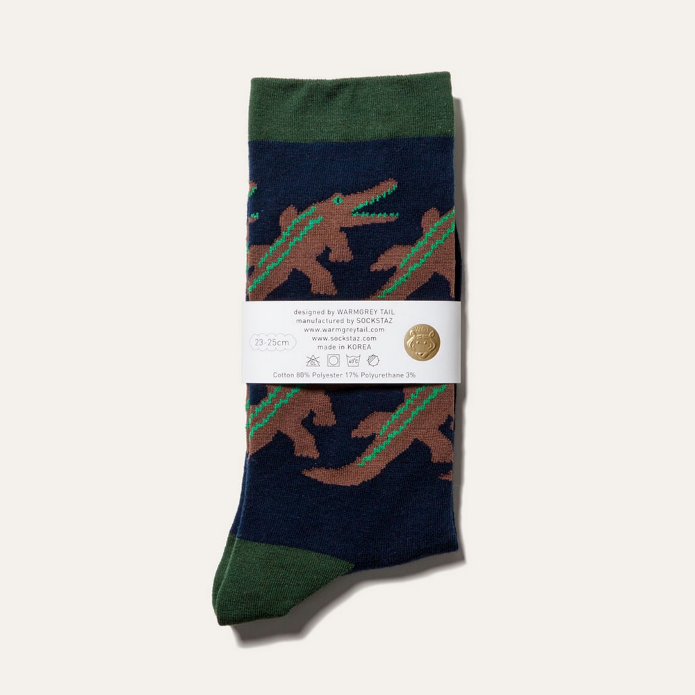 Socken Crocodile in Navy mit Krokodilen auf blau, gruenem Stoff in Produktverpackung.