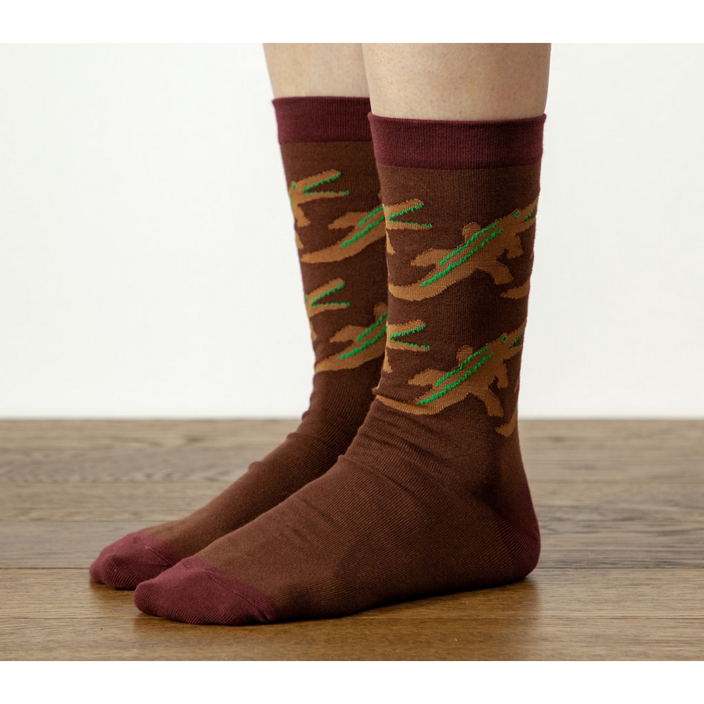 Fuesse in Warmgreytail Socken Crocodile Brown auf Holzboden vonschraeg vorn.