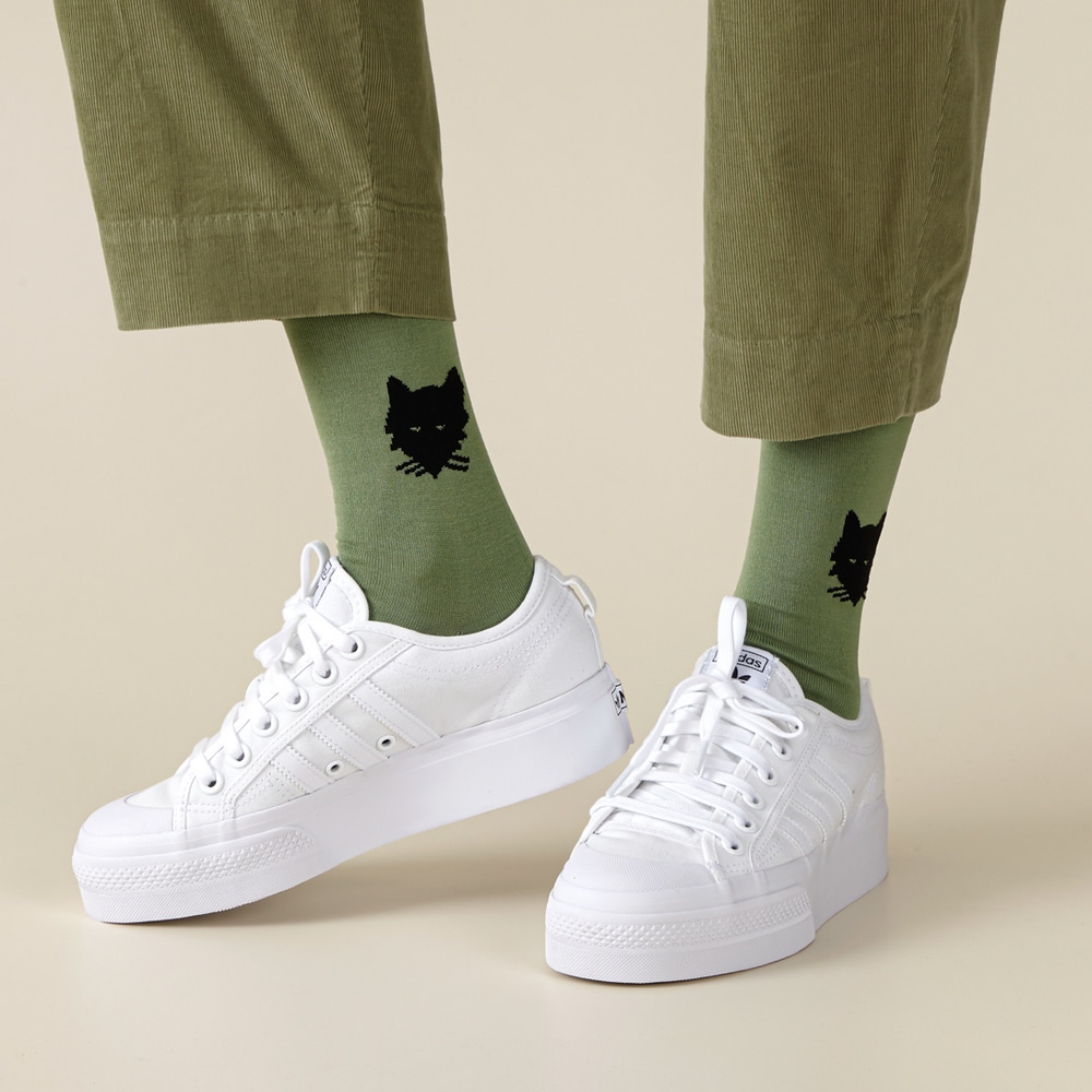 Warmgreytail Socken Wolf Olive mit schwarzem Wolfskopf, kombiniert mit gruener Hose und weissen Turnschuhen.