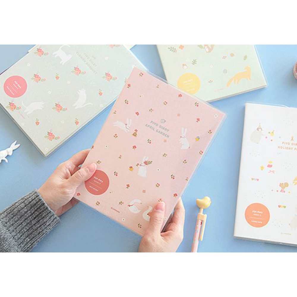 Verschiedene Piyo Diaries auf dem Tisch und inden Haenden einer Person das Piyo April Garden Pink.
