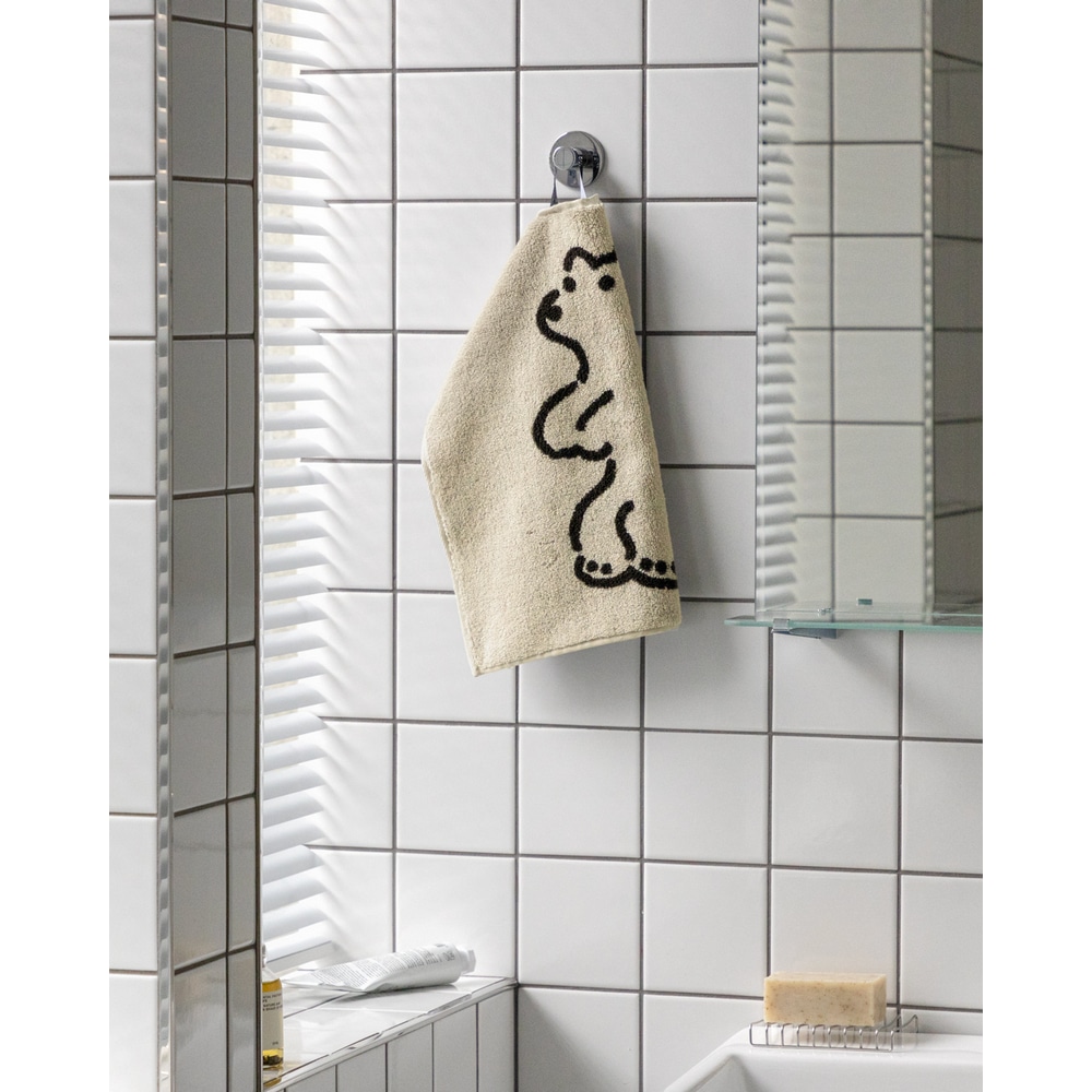 Warmgreytail Frottier Handtuch klein, Huggy Bear Cream neben Spiegel in weiss gekacheltem Badezimmer.