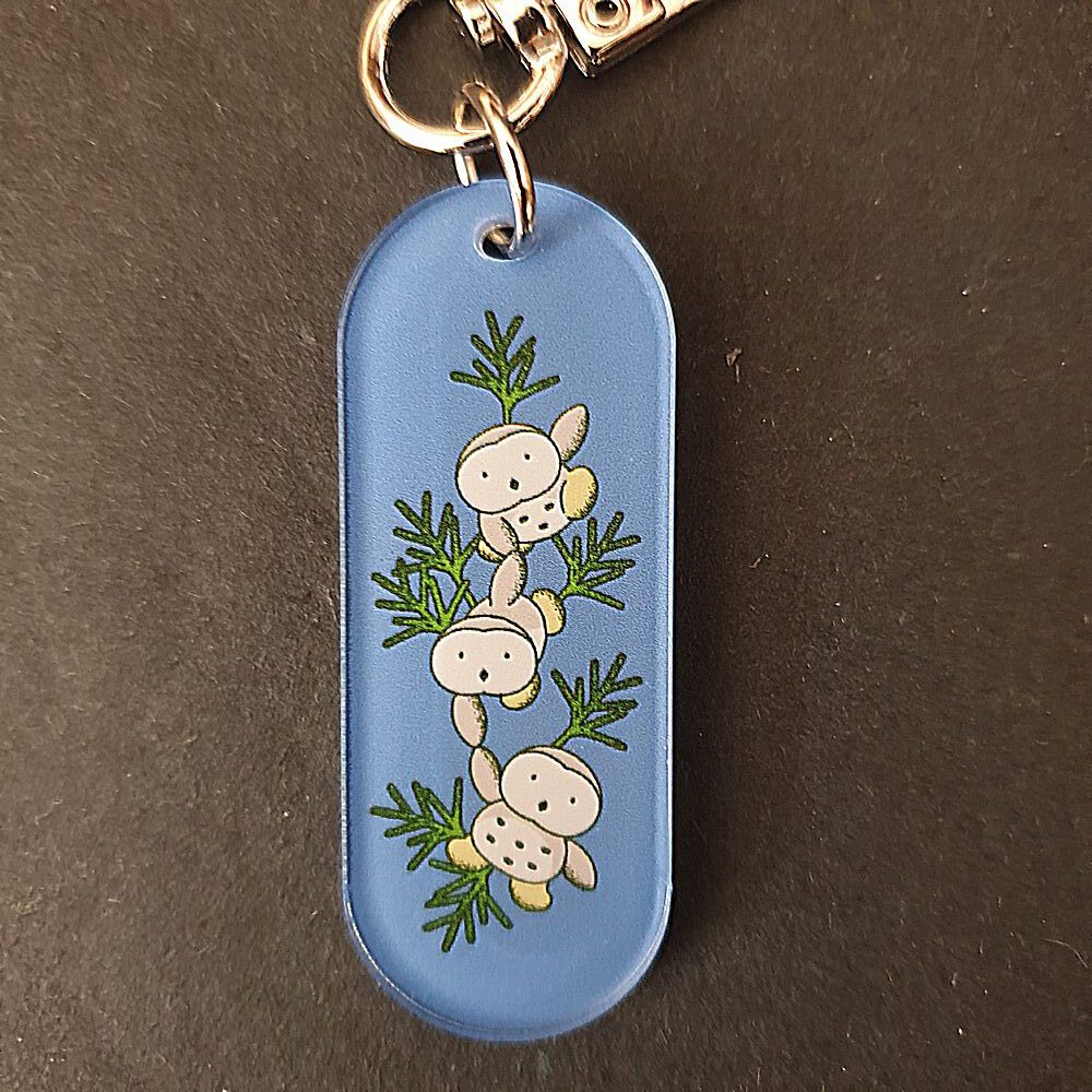Ovaler, blauer Schluesselanhaenger aus Acryl, acrylic keyring von Naive Garden, mit Motiv von drei kleinen und suessen Eulen auf gruenen Zweigen.