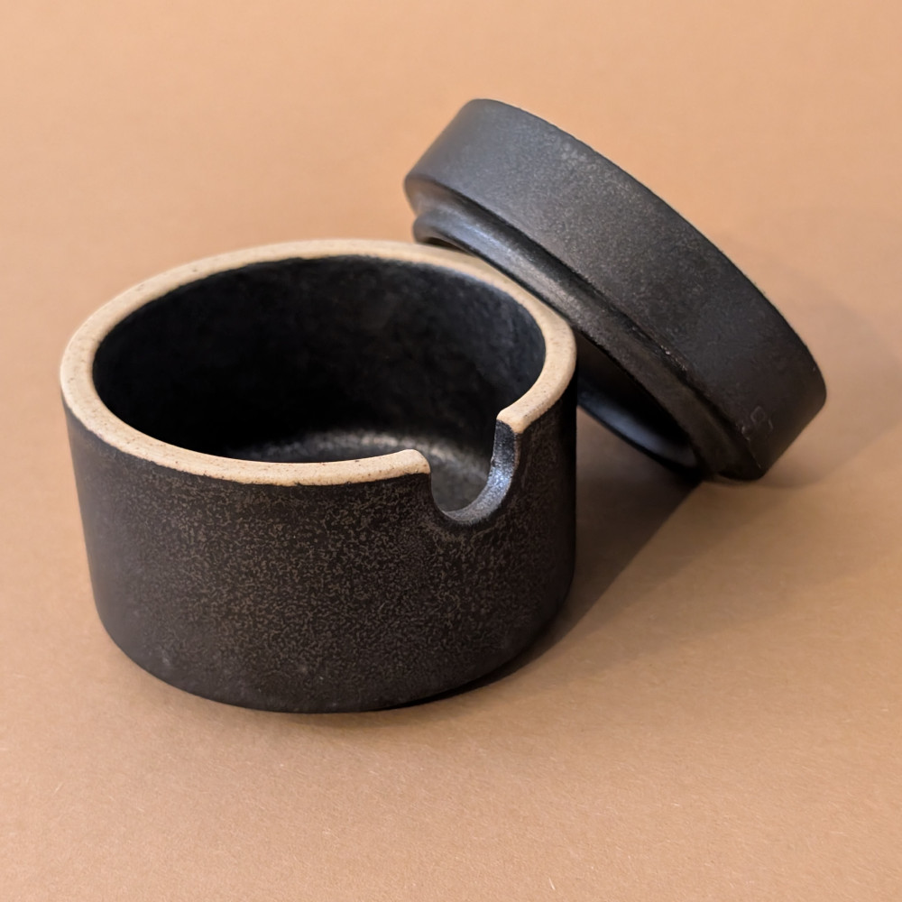 Handgemachte schwarze Sauce bowl in der Groesse S von Mukyung. Der passende Deckel lehnt daneben.